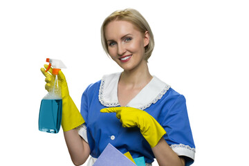 Housekeeper in uniform, yellow rubber gloves spray on white background. Smiling maid pointing at bottle of spray.