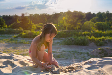 Little girl on the beach making a sand castle at sunset.