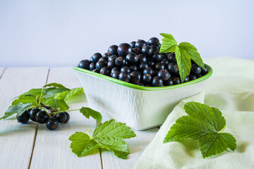 Ripe black currant berries in a bowl on a white wooden table