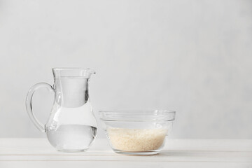 Bowl with rice and water in jug on table