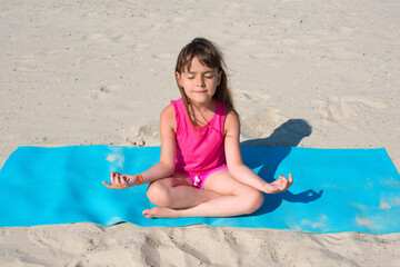 Little girl does yoga on the beach. The concept of sport and active play in the summer. Beach gymnastics.
