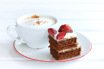 piece of chocolate cake with strawberries and a white cup of frothy cappuccino on a plate. delicate sweet dessert and coffee