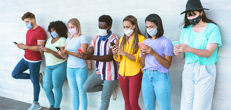 Young people wearing face safety masks using smart mobile phones while keeping social distance during coronavirus time - Technology and covid-19 spread prevention concept Focus on right girls hands