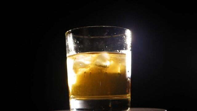 Close-up of a misted-up glass of whiskey with ice slowly spinning around on black background. The concept of the celebration and alcohol.