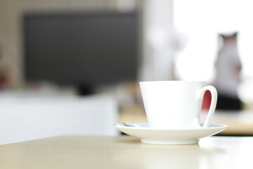 White ceramic cup of hot coffee or tea on wooden computer desk with natural light in the morning at office. Caffeine drinks cause a fresh feeling.