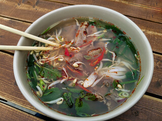 Close-up of a deep plate with Vietnamese pho bo soup and chopsticks on a wooden table. Meat broth...