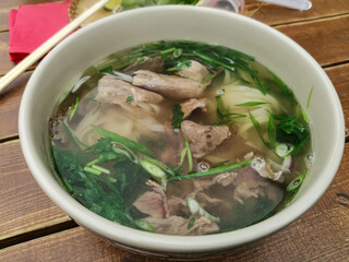 Deep plate with beef broth and herbs on a wooden table. Basis for Vietnamese pho bo soup. Lunch at a street cafe. Traditional Asian cuisine.
