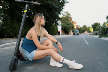 Fototapeta na wymiar Young beautiful girl is sitting on her electro scooter in the summer on the street