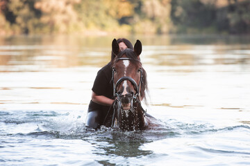 Pferd und Frau schwimmen im See frontal auf eine Kamera zu