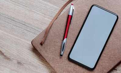 Mockup blank screen  smartphone with pen and diary on wooden table, copy space.