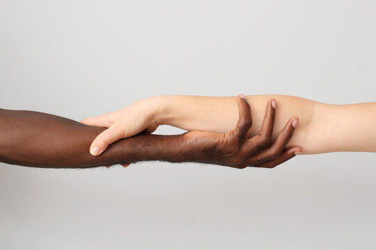 Caucasian woman and African-American man holding hands together on light background. Racism concept