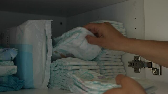 hand taking a disposable diapers from the cupboard drawer
