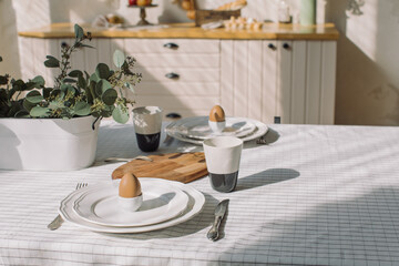 Table served with plates, coffee cups and eggs for breakfast at modern kitchen. Family time, Easter celebration concept.