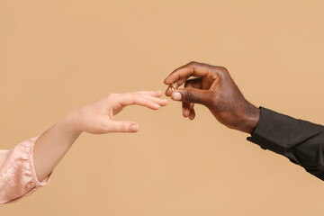 African-American man putting wedding ring on finger of Caucasian woman against color background. Racism concept - Powered by Adobe