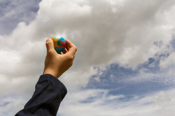  Boy's hand holding little globe against sky 