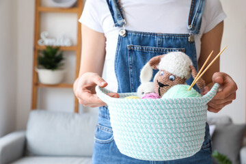 Woman holding wicker basket with toys and knitting yarn in room