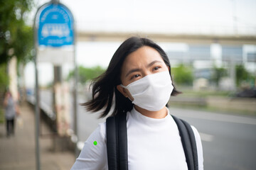 Asian woman wearing protective face mask standing at bus stop. New lifestyle with Corona Virus COVID-19.