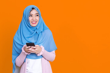 Smiling Asian muslim woman with using mobile or smartphone exciting over isolated color background.