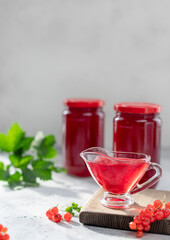 natural organic red currant jam in a sauceboat on the background of jars with jam and fresh berries with green leaves. Healthy food for breakfast. copy space. vertical image. Gray background