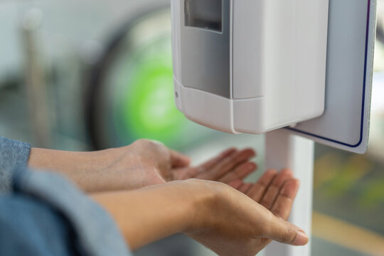 Close up of woman holding hands under automatic sanitiser dispense
