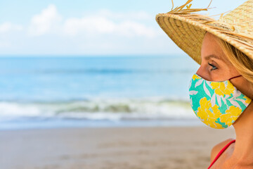 Funny portrait of young woman in straw hat on tropical sea beach. New rules to wear cloth face covering mask at public places due coronavirus COVID 19. Family holiday with kids, travel at summer 2020.