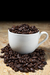 Roasted coffee beans in a white coffee cup on a fragrant wooden table.
