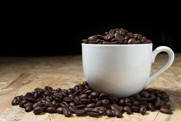 Roasted coffee beans in a white coffee cup on a fragrant wooden table.