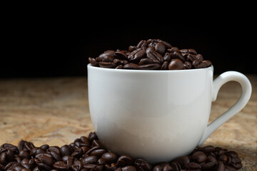 Roasted coffee beans in a white coffee cup on a fragrant wooden table.
