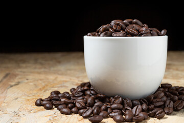 Roasted coffee beans in a white coffee cup on a fragrant wooden table.
