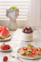 Trendy home breakfast with tiny pancakes and strawberry on white table. 
