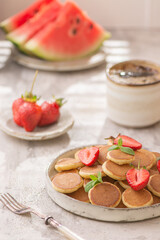 Trendy home breakfast with tiny pancakes and strawberry on white table. 