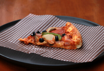 A piece of triangle Pizza  place on brown scotch paper  in the black round plate.