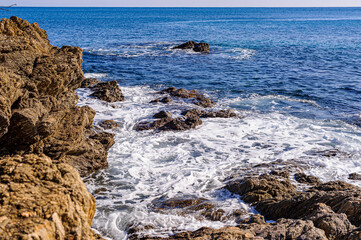 Mediterranean shore in the south of France. The red rocks of the Esterel descend into the sea. Waves breaking on the rocks cause a white foam.