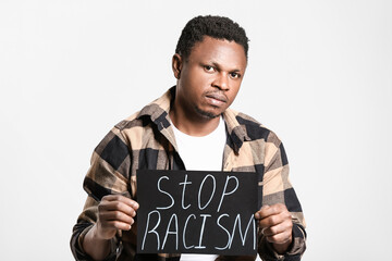 Sad African-American man with poster on light background. Stop racism