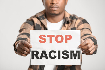 Sad African-American man with poster on light background. Stop racism
