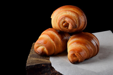 Golden croissants of yeast dough on the edge of the wooden table against black background