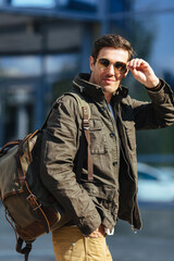 Waist portrait of confident casual man in olive green jacket in sunglasses in the city.