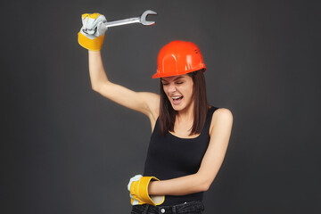 beautiful women in an orange helmet. holding a spanner in his hand. Posing while working, twisting an imaginary bolt..