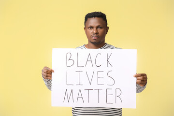 Sad African-American man with poster on color background. Stop racism
