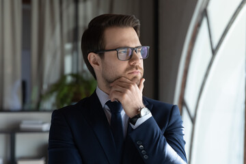 Pensive caucasian businessman in glasses and formal suit look in window distance thinking pondering, thoughtful male employee or boss lost in thoughts, planning considering company problem solution
