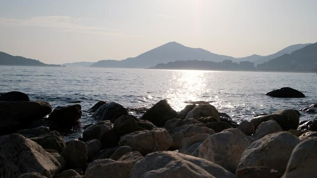 Seashore at sunset with rocks in the foreground and mountains in the background. The sun's rays are reflected in the water. Beach of Kamenovo in Montenegro at sunset