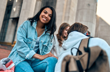 Attractive African American girl student sits on the steps near the campus with her friends.