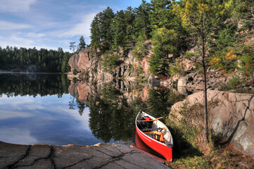 Red canoe on shoreline of George Lake Killarney Park with forest and rocks