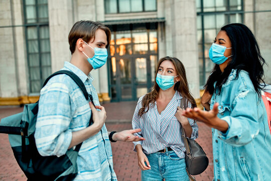 A group of students wearing protective medical masks talk outside the campus.