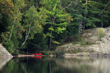 Red canoe on shoreline of George Lake Killarney Park with forest and rocks