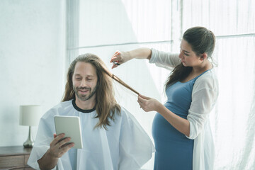 Pregnant woman cutting hair her husband during quarantine and pandemic coronavirus at home