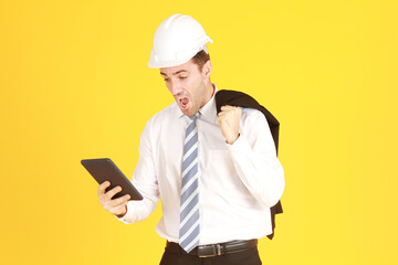 Handsome and smart engineer in suit and white shirt and Wearing a white safety engineering hat with hand holding smartphone Surprised and stressed with work isolated on yellow background.