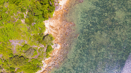 Aerial view of the rocky coast near the blue lagoon of Port Dickson, Malaysia. Directly above the shore. Waves hit the stones in the water.  Sun reflecting in the crystal clear water .
