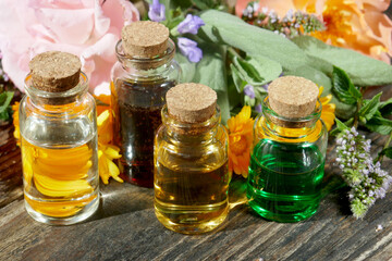 Selection of  glass aromatherapy essential oil bottles, with herbs and flowers in the background