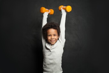 Happy strong black child boy holding dumbbells